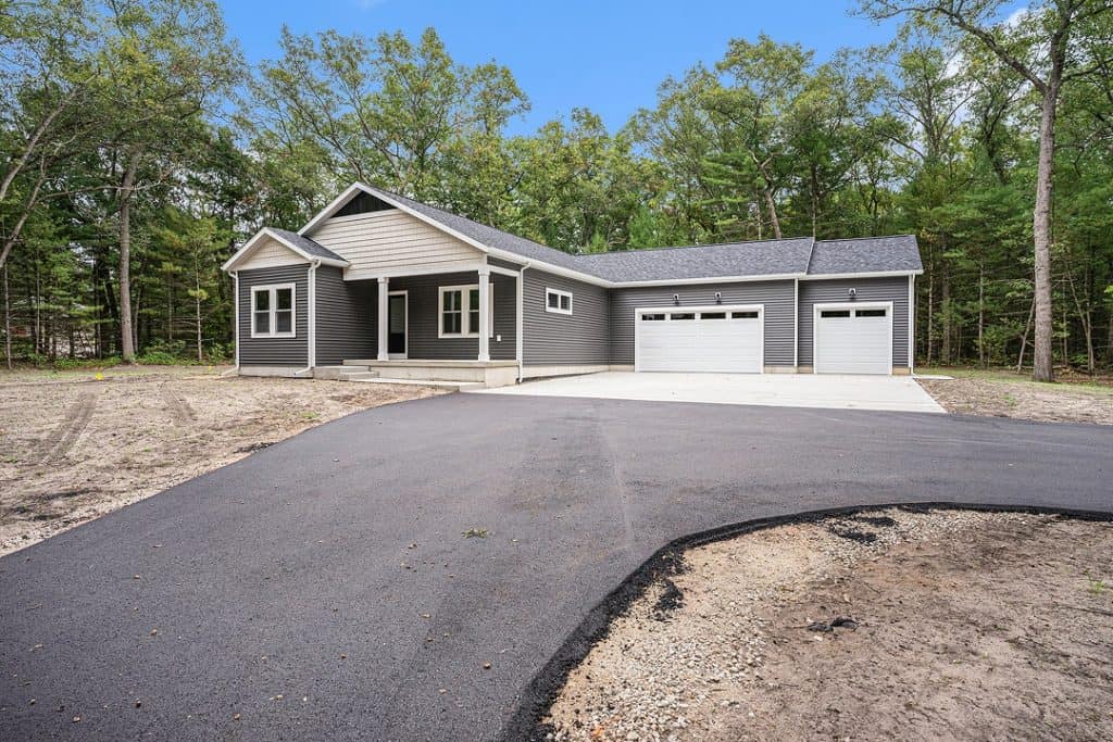 New custom-built home with gray siding and three-car garage in a wooded area.