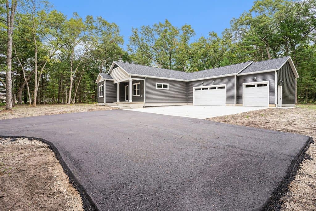 New modern house with three-car garage and paved driveway in a wooded area.