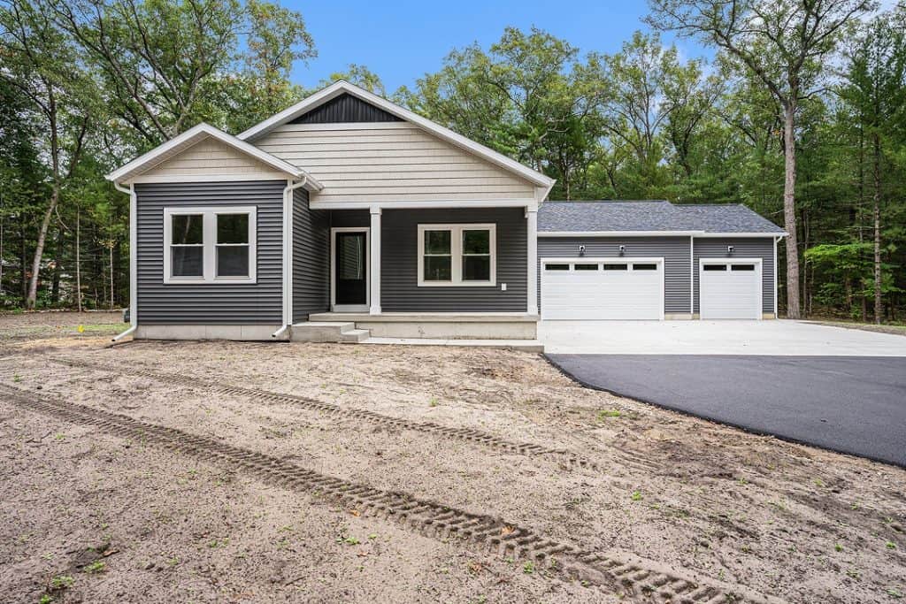 New custom home with gray siding and attached garage in a wooded area.