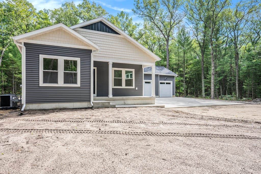 Newly built modern home with gray siding and attached garage in a wooded area.