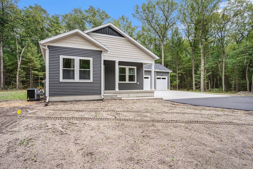 Newly built modern home with gray siding and white trim in a wooded area.