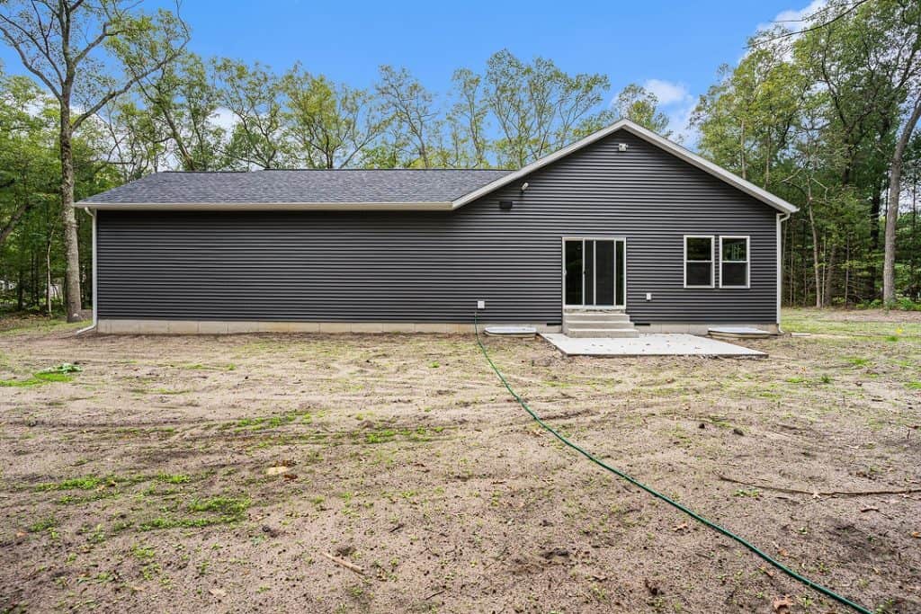 Newly built modern home with dark siding and large windows in a wooded area.