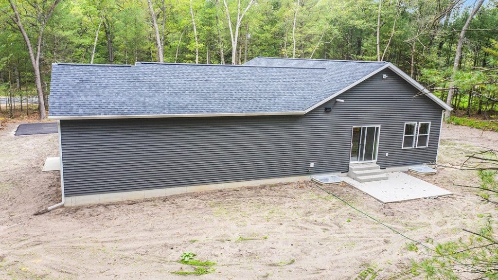 Modern gray custom home with large backyard and wooded surroundings.