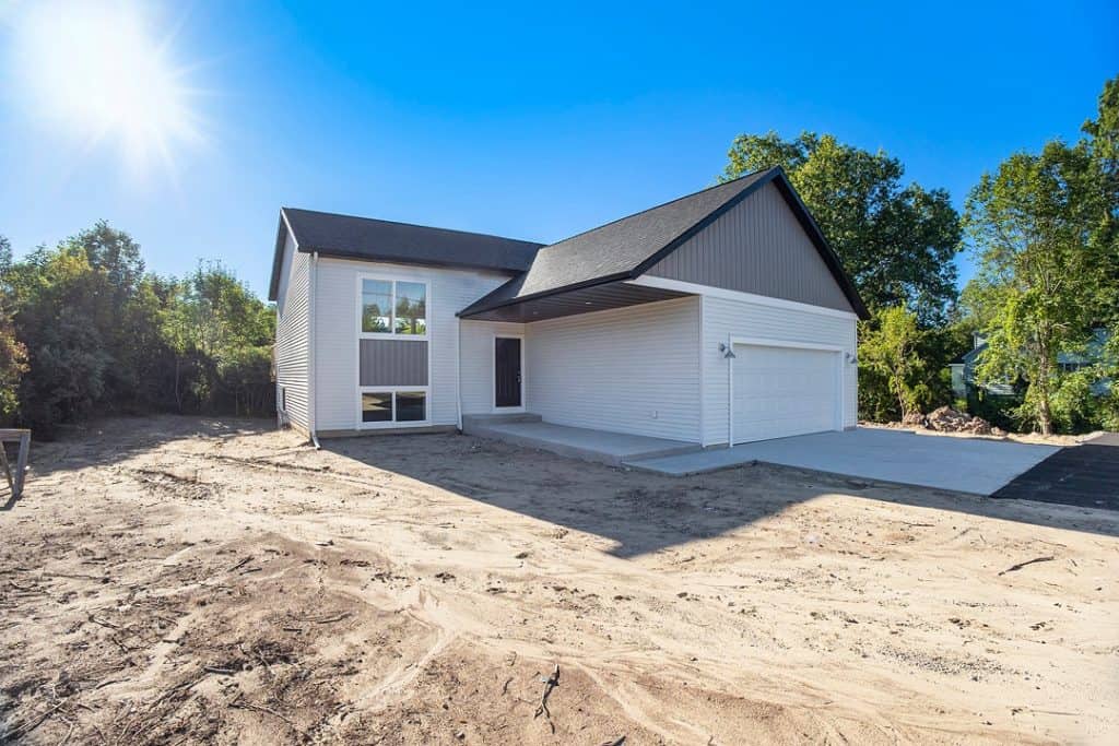 Newly built modern home with white siding and black roof in a sunny setting.