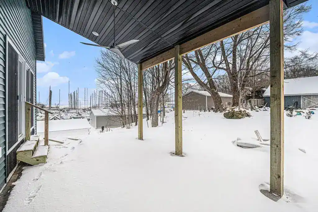 Snow-covered backyard patio with wooden support beams and trees in winter.