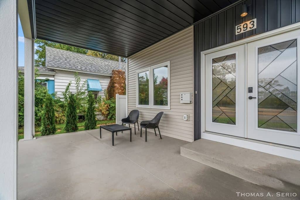Contemporary house entrance with covered porch, two chairs, and a small table.