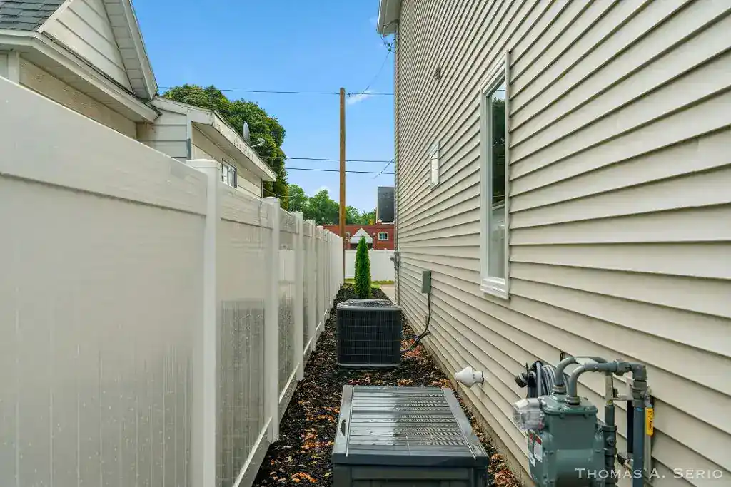 Side view of a house with beige siding and white fence, HVAC units, and utility meters.