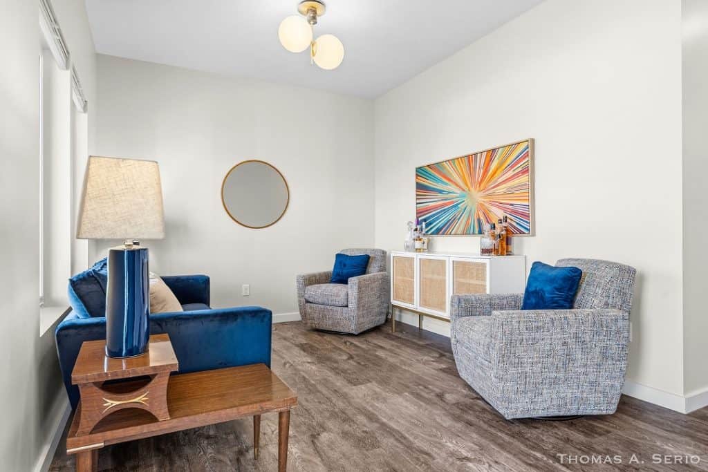 Contemporary living room with blue and gray armchairs, artwork, and wooden flooring.