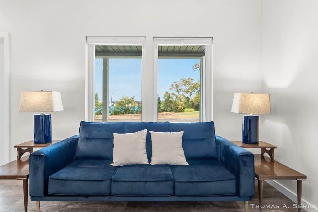 Stylish living room with blue sofa, white pillows, and large windows.