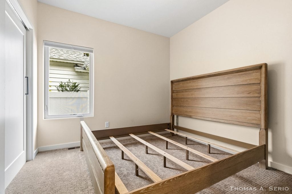 Empty bedroom with wooden bed frame and window view.