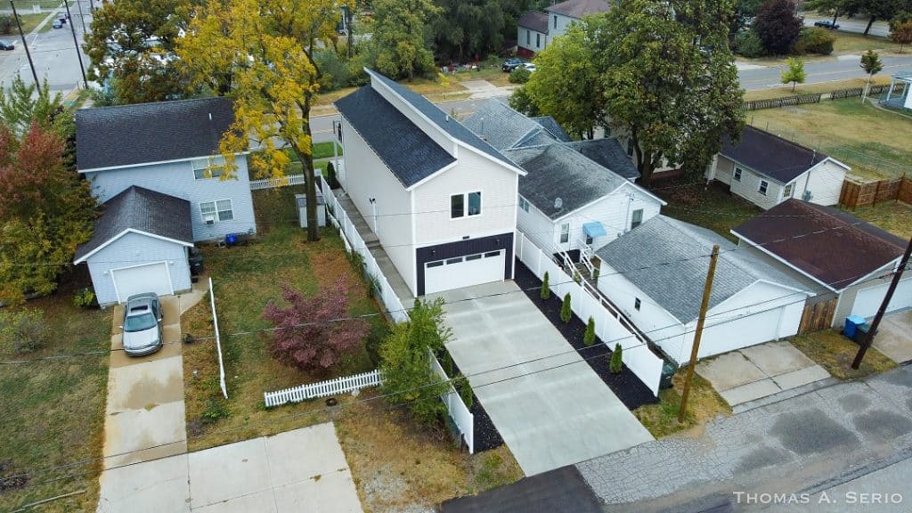 Aerial view of a modern custom home with a large driveway and landscaped yard.