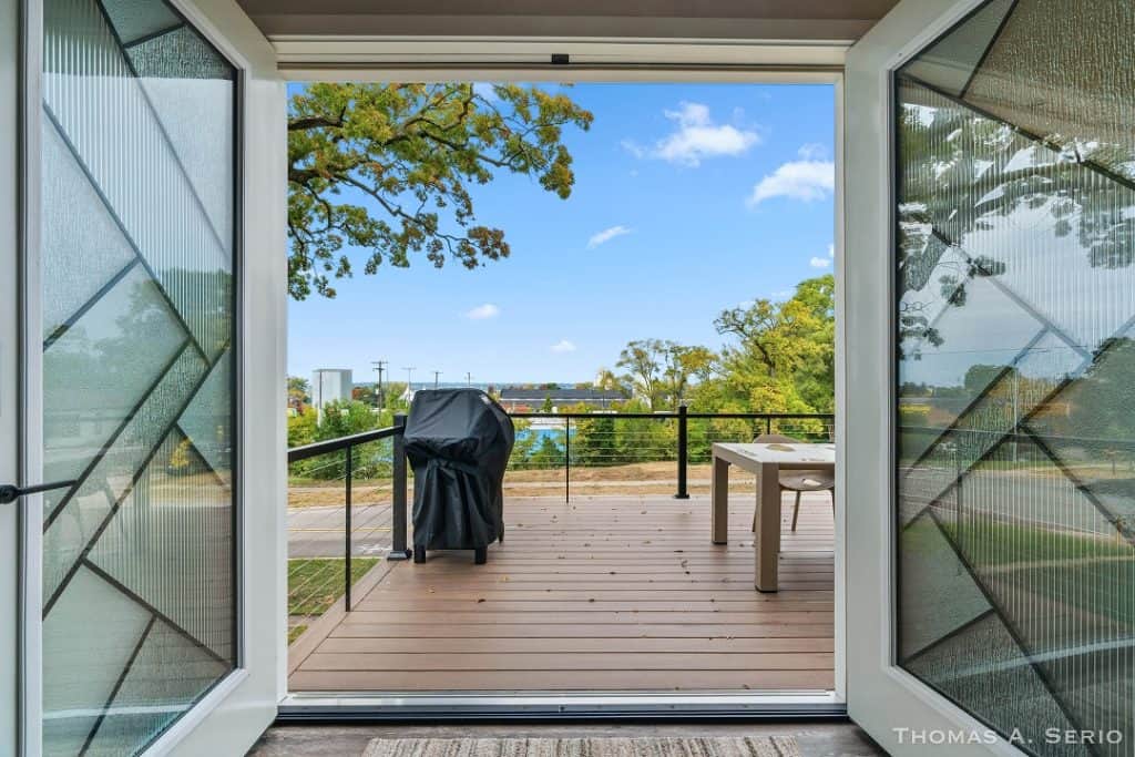 Balcony with grill and table overlooking trees and blue sky.