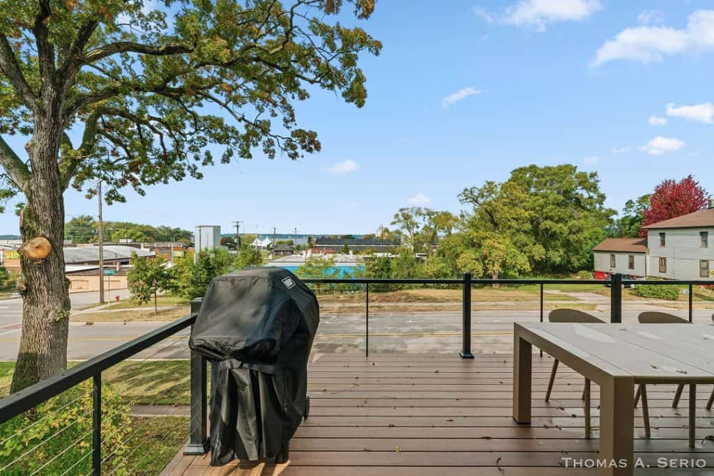 Outdoor deck with barbecue grill and scenic view of trees and sky.