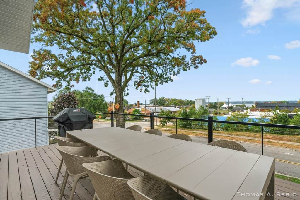 Outdoor deck with dining table and chairs overlooking a tree and neighborhood.