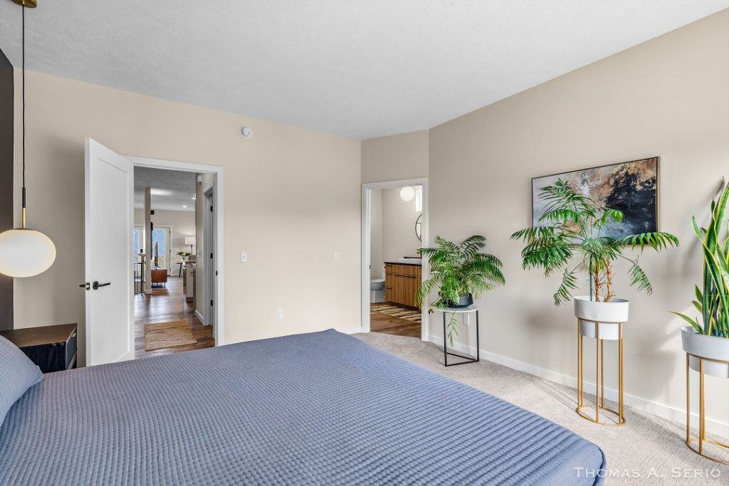 Bright bedroom with beige walls, large window, and indoor plants.