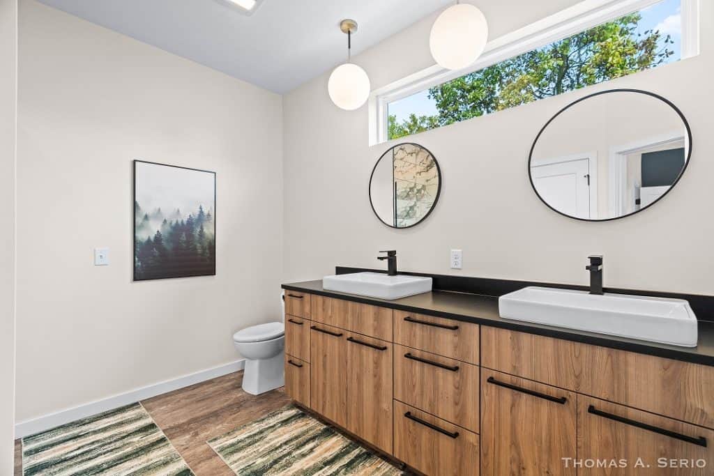 Contemporary bathroom with dual sinks, round mirrors, and natural light.