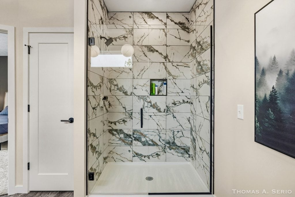Modern walk-in shower with marble tiles and glass enclosure.