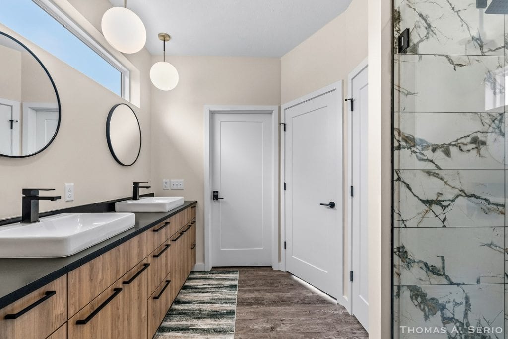 Contemporary bathroom with dual sinks, wooden cabinetry, and marble shower.