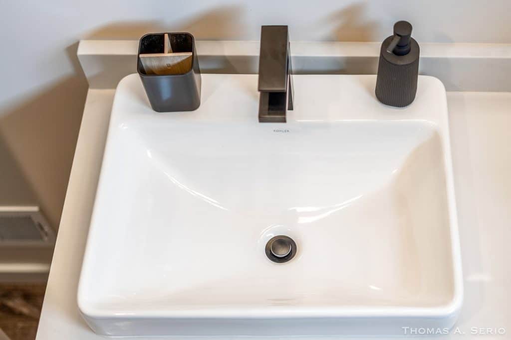 Contemporary bathroom sink with black soap dispenser and toothbrush holder.
