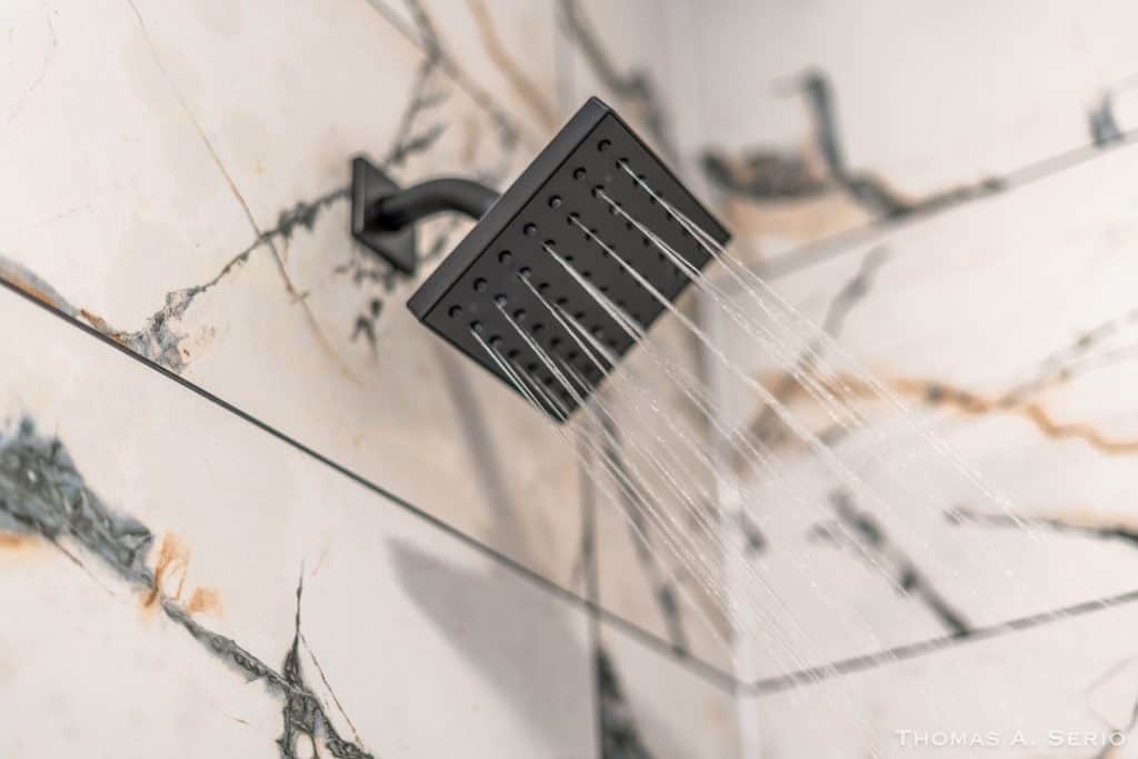 Black square shower head with water flowing in a marble bathroom.