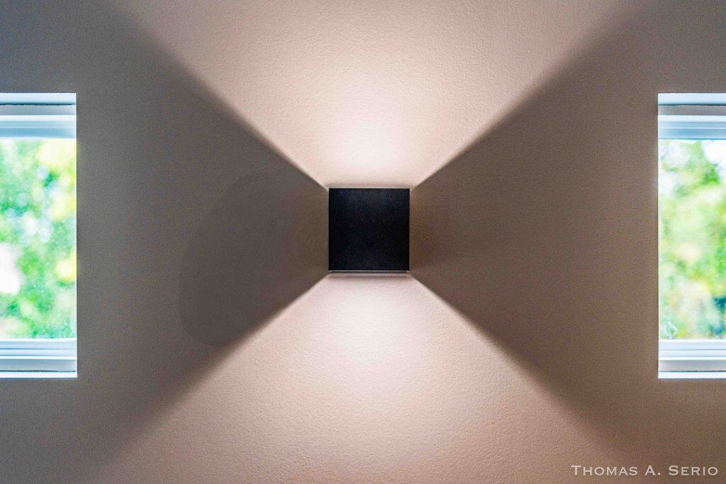 Contemporary wall light casting symmetrical shadows between two windows.