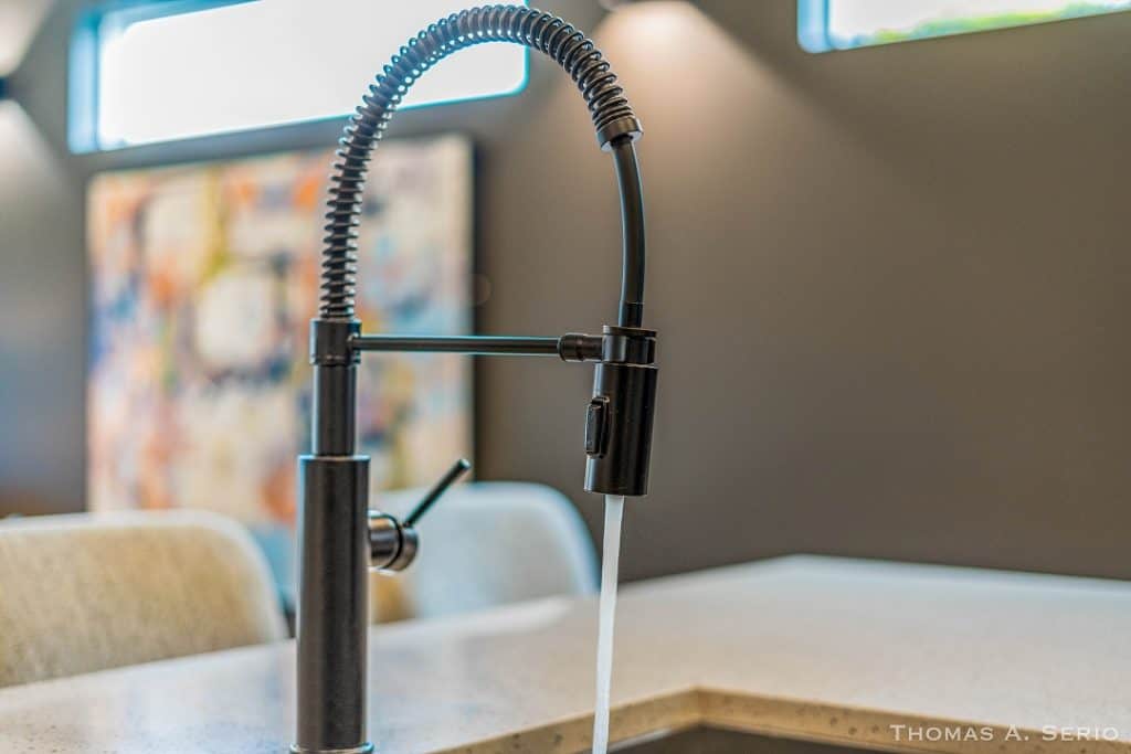 Sleek black kitchen faucet with water running in a contemporary kitchen setting.