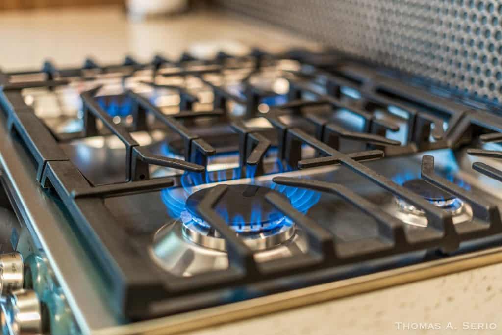 Close-up of a modern gas stove with blue flames in a custom home kitchen.