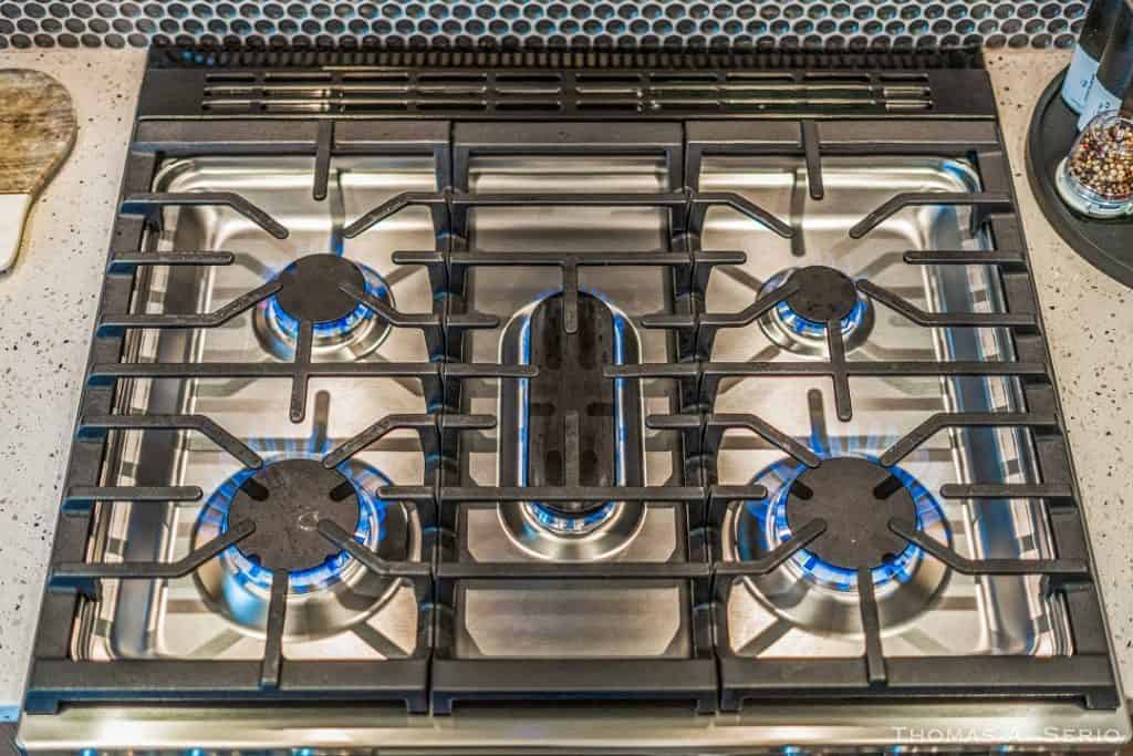 Stainless steel gas cooktop with five burners and blue flames.