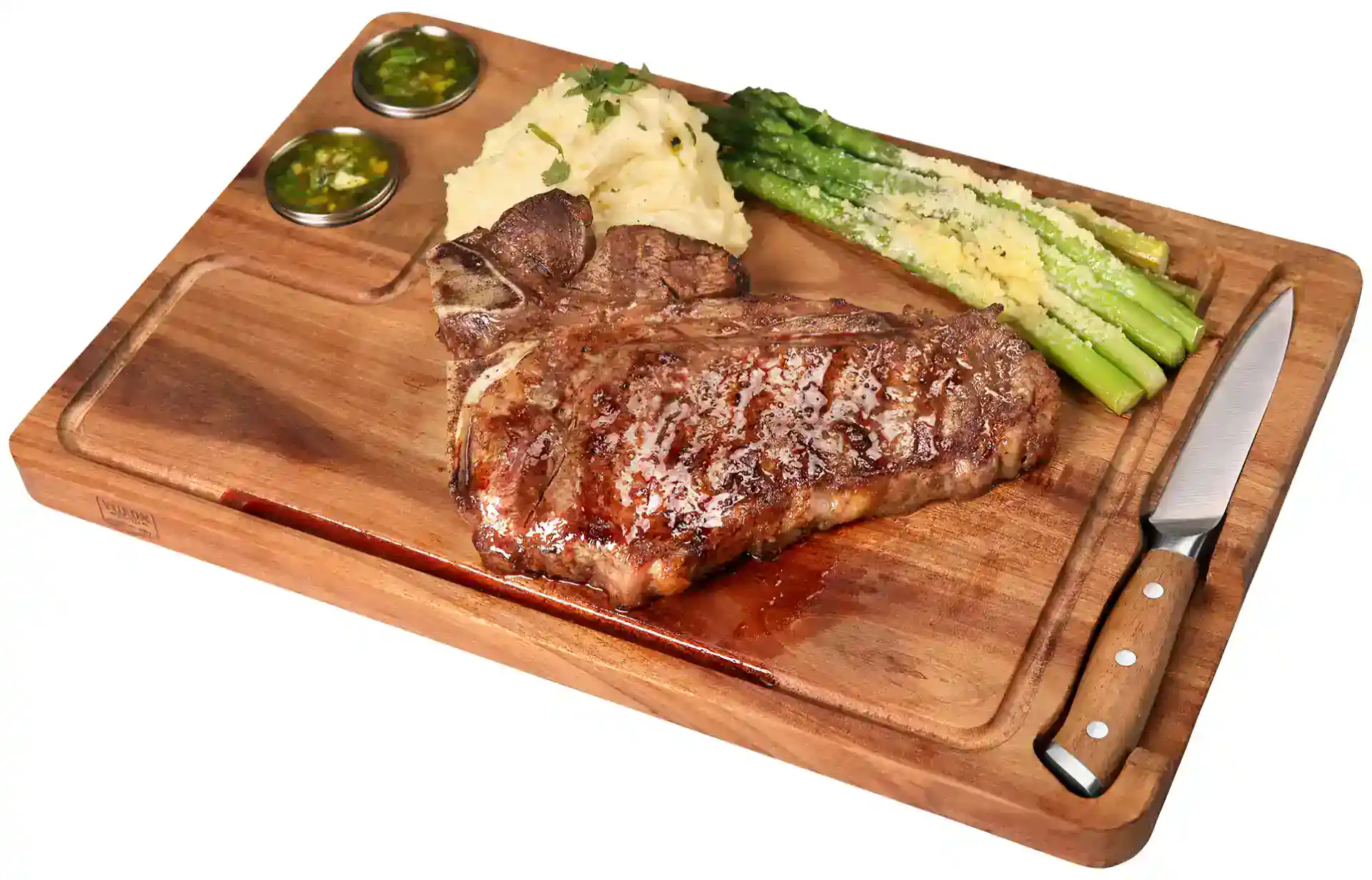 Juicy grilled ribeye steak served with asparagus, mashed potatoes, and two dipping sauces on a woode.