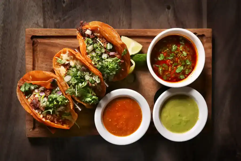Baja shrimp tacos with salsa, guacamole, and dipping sauces on a wooden tray.