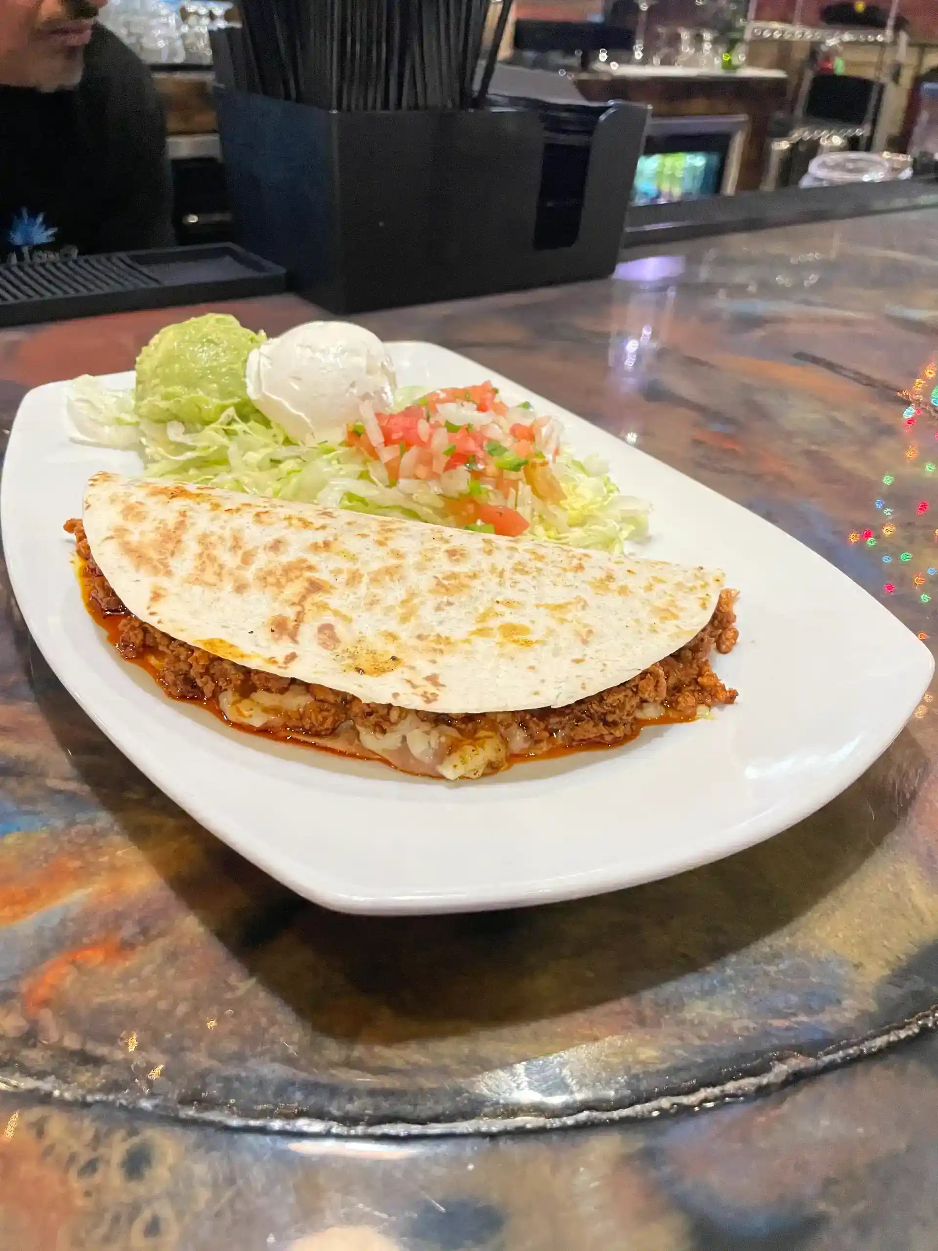 Cheeseburger taco served with lettuce, sour cream, and salsa on a white plate.