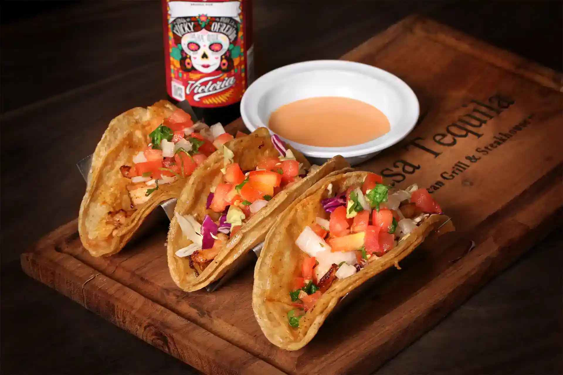 Tacos with fresh salsa and a side of hot sauce on a wooden serving board.