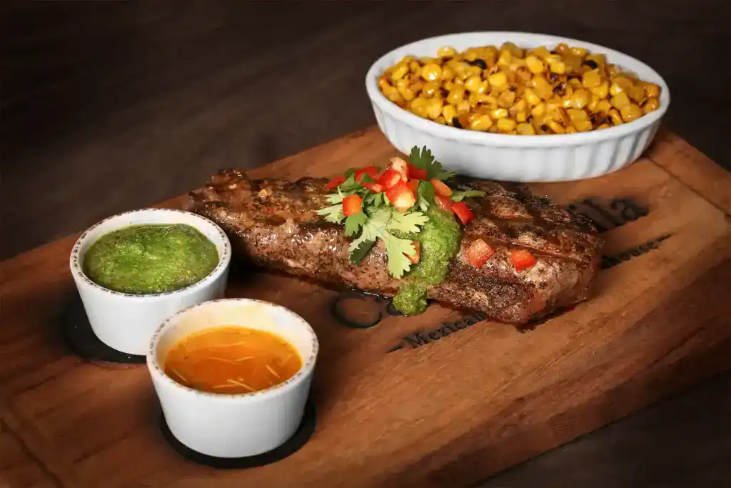 Grilled fish served with corn, green sauce, and orange sauce on a wooden board.