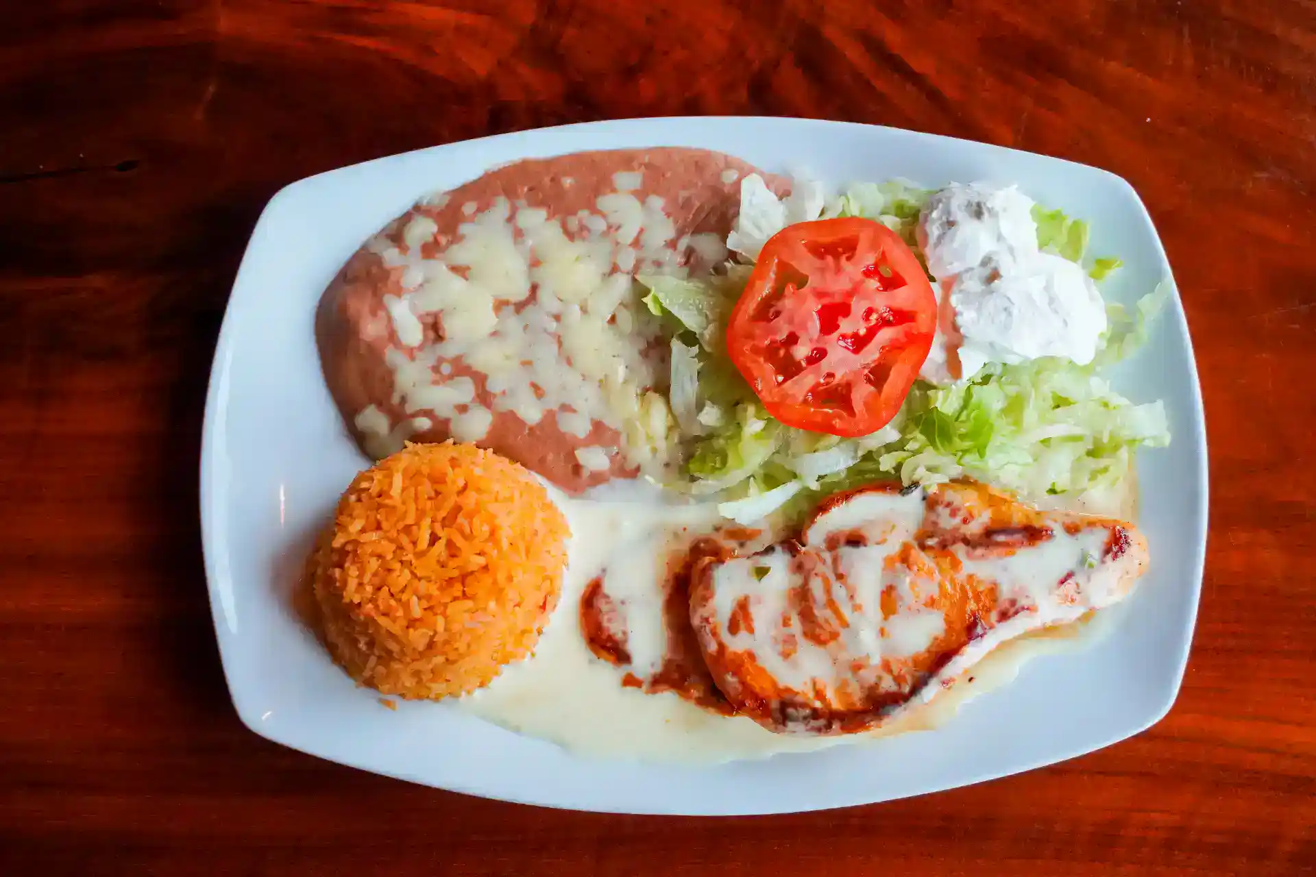 Traditional Mexican dish with rice, beans, chicken, and salad on a white plate.