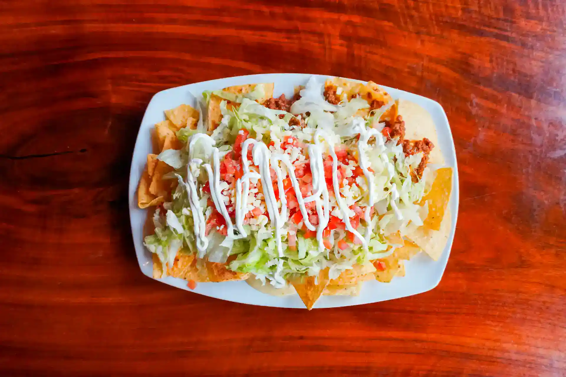 Fresh Mexican Nachos with lettuce, cheese, and sour cream on a white plate.