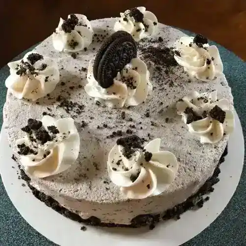Delicious Snickers cake with Oreo decorations, whipped cream, and cookie crumbles, perfect for special occasions.