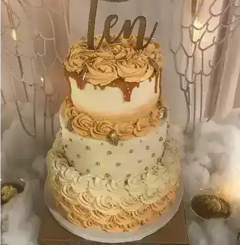 Beautiful three-tier cake decorated with beige and white frosting, gold accents, and a "Len" topper, perfect for special occasions and events.