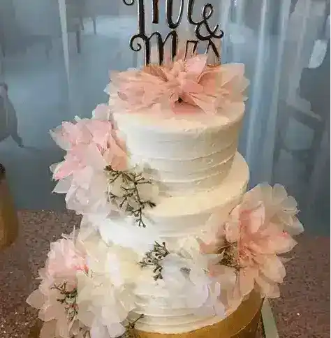 Elegant three-tier white wedding cake decorated with pink and white flowers for special occasions.