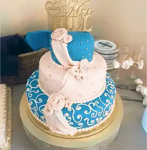 Decorative heart-shaped wedding cake featuring pink roses, blue fondant, and intricate white piping details, perfect for special celebrations.