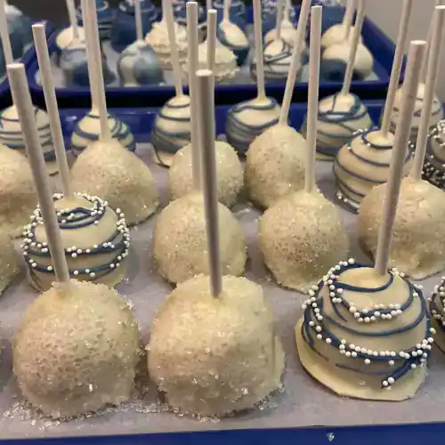 Assorted white chocolate cake pops with sprinkles and decorative drizzle, perfect for celebrations.