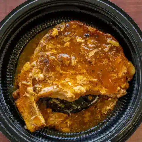 Juicy smothered pork chops with rich gravy served in a black takeout container, showcasing Southern soul food cuisine. Perfect for comfort food lovers.