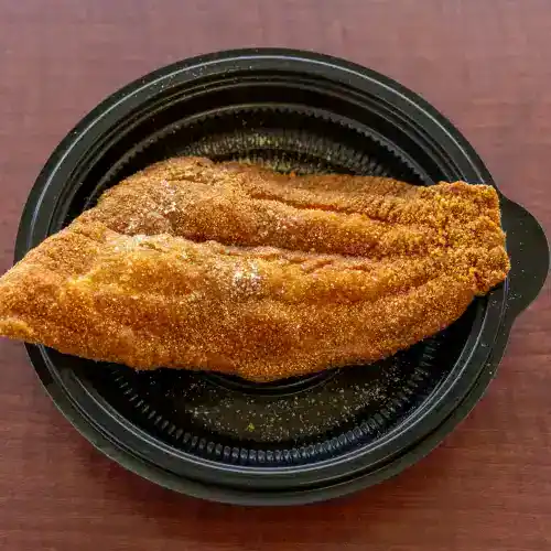 Delicious fried catfish fillet with golden, crunchy breading served on a black plate. Perfect for seafood lovers seeking flavorful, Southern-style soul food.