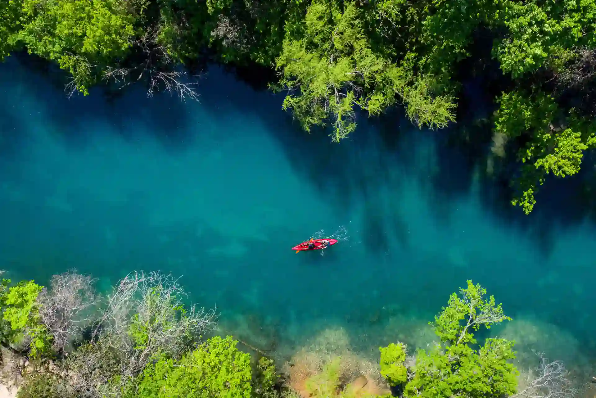 Aerial view of a person kayaking in a narrow, clear blue river surrounded by dense green trees, reminiscent of the serene escapes nonprofit lawyers dream about in their quest to guide nonprofit organizations.