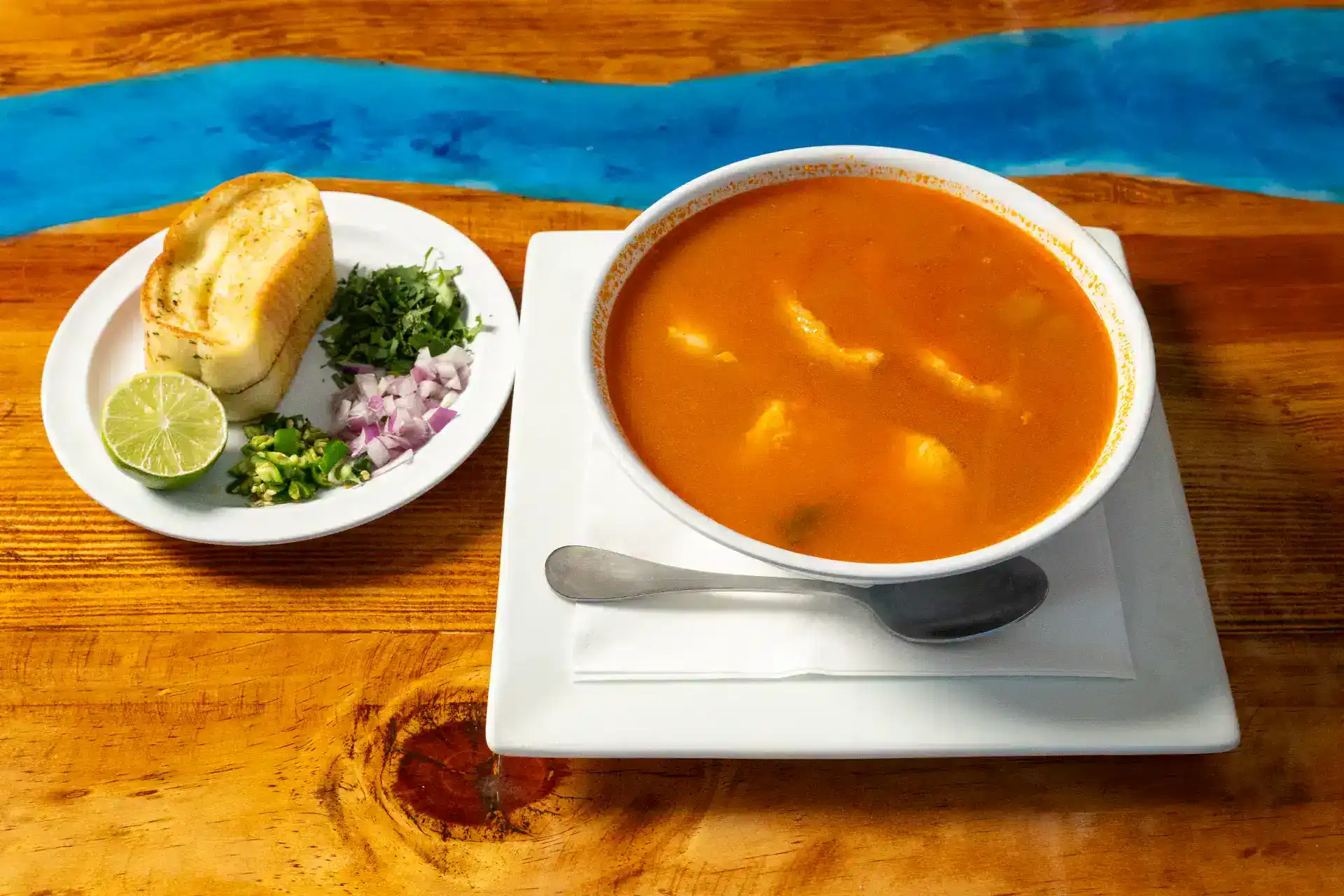Traditional fish soup served with lime, bread, and herbs on a wooden table.