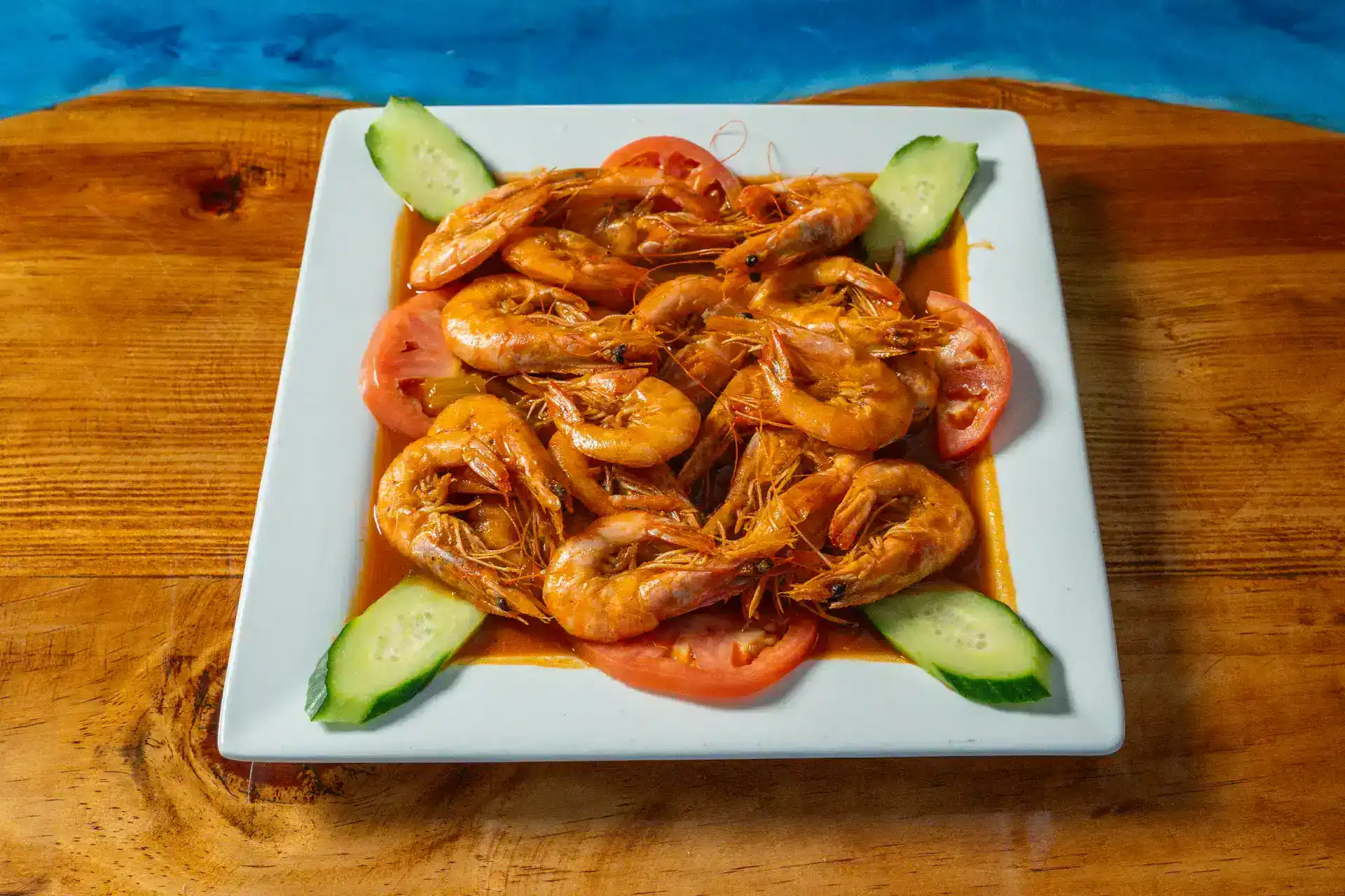 Spicy shrimp dish with cucumber and tomato slices on a white plate.