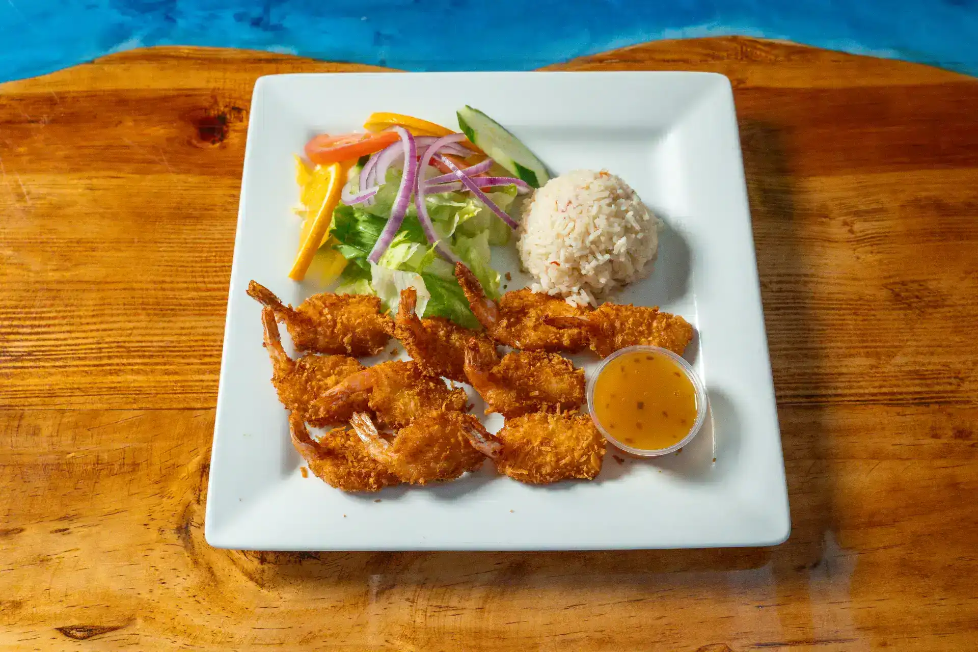 Coconut shrimp served with mango salsa and dipping sauce on a white plate.