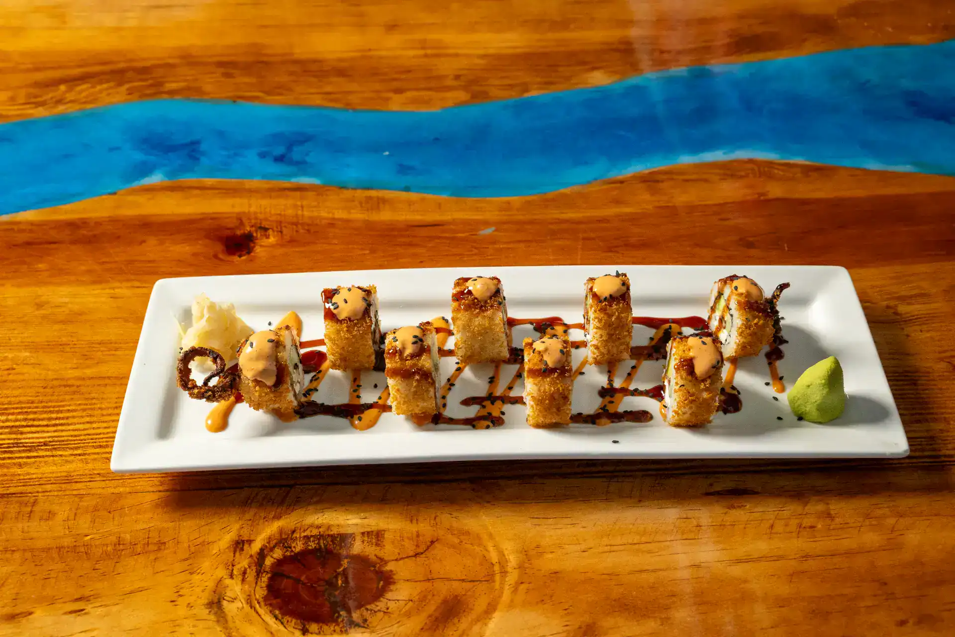 Sushi roll with octopus and sauce on white rectangular plate.