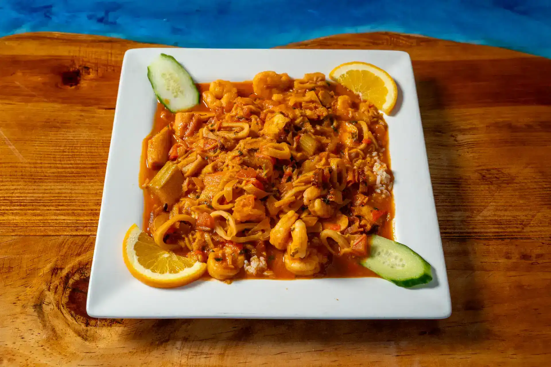 Seafood rice dish with lemon and cucumber garnishes on a white plate.