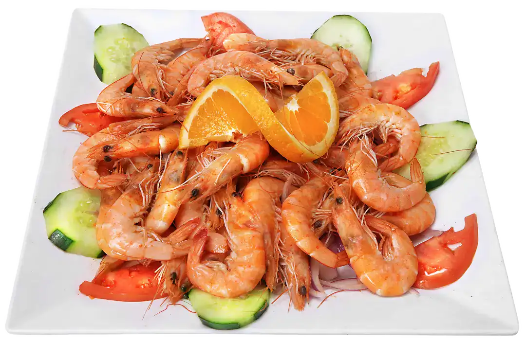 Steamed shrimp served with orange slices and cucumber on a white plate.