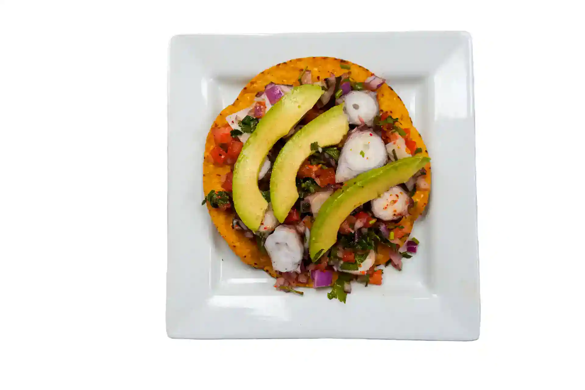 Shrimp tostada with avocado, onions, and cilantro on a white plate.
